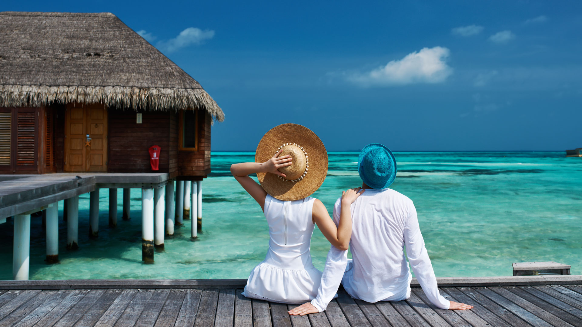 couple sitting on a pier looking at a cabana